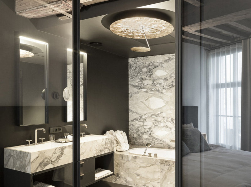Hotelzimmer mit Bad und Schlafraum - Marmorfliesen und Deckenleuchte Lederam C150 von Catellani & Smith.